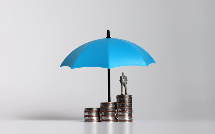 Miniature businessman standing on a pile of coins with umbrella