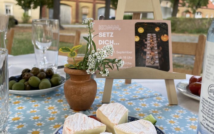 Foto eines gedeckten Tisches mit Käse- und Obstteller im Freien vor einer Backsteinkirche
