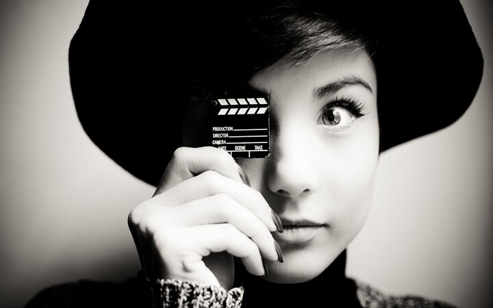 Schwarz-weiß-Foto einer jungen Frau mit Miniatur-Filmklappe vor einem Auge