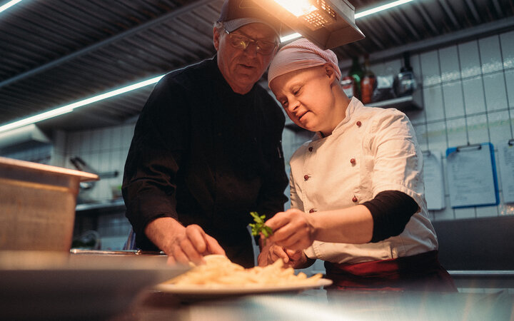 Eine Frau mit Down-Syndrom und ein Mann bei der Arbeit in einer Gastronomie-Küche
