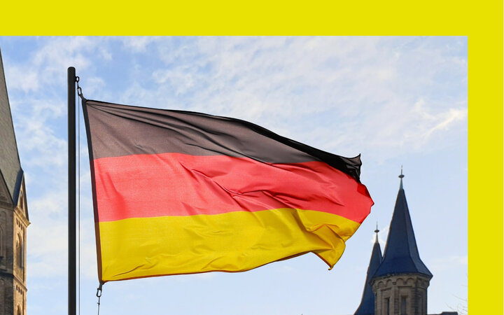 Foto einer Deutschlandflagge mit mehreren Türmen einer großen Kirche