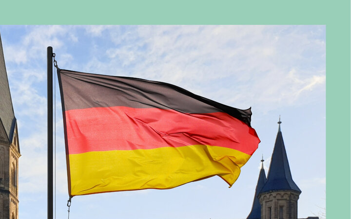 Foto einer Deutschlandflagge vor mehreren Türmen einer großen Kirche