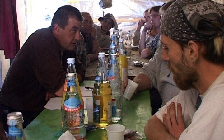 Menschen in Arbeitskleidung an einem Biertisch mit Wasser- und Saftflaschen auf einer Baustelle
