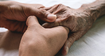 Hands of the old man and a young man on a white bed in a hospital