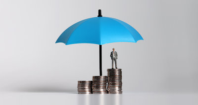 Miniature businessman standing on a pile of coins with umbrella