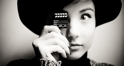 Schwarz-weiß-Foto einer jungen Frau mit Miniatur-Filmklappe vor einem Auge
