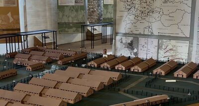 Modell einer Lageranlage, im Hintergrund eine Landkarte Mitteleuropas mit markierten Orten